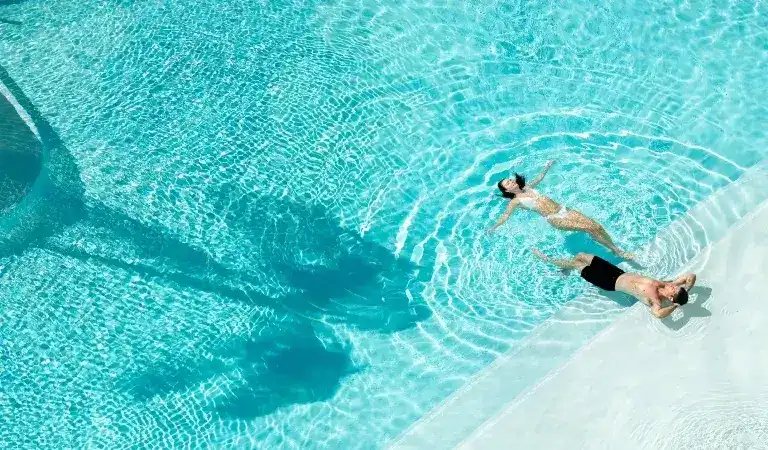 A Couple on sunlounges by a stunning turquoise pool.