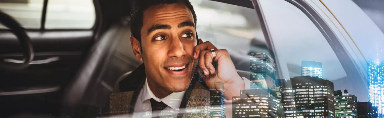 A man speaking on a phone in a car with a cityscape visible outside.